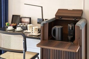 Ett litet, praktiskt kök med en kaffebryggare, vattenkokare och en liten matplats med en stol och ett bord.