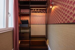 A narrow hallway with a staircase leading to a room with patterned wallpaper and a bed.