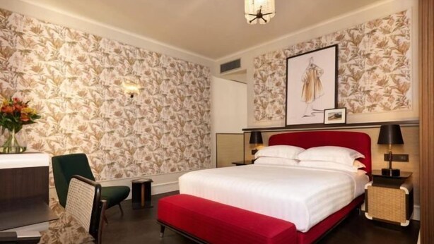 Una habitación de hotel con una cama grande, un escritorio, una silla y un banco rojo.
