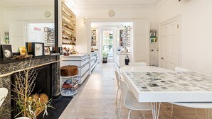 A spacious kitchen with white cabinetry, a marble countertop, and a dining area with a white table and chairs. - Listed Georgian Home w/ Contemporary Architecture (London)
