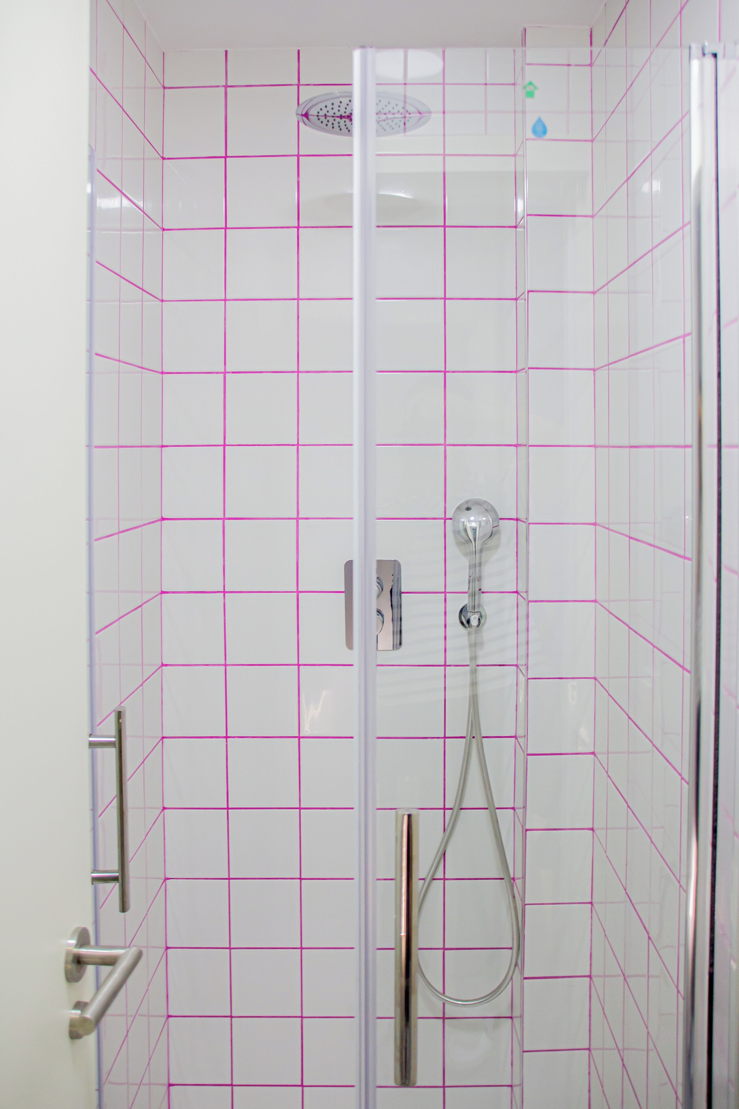 Une cabine de douche fermée par des parois en verre, avec un mur recouvert de carreaux disposés en motif quadrillé, une douchette à main et un panneau de commande.