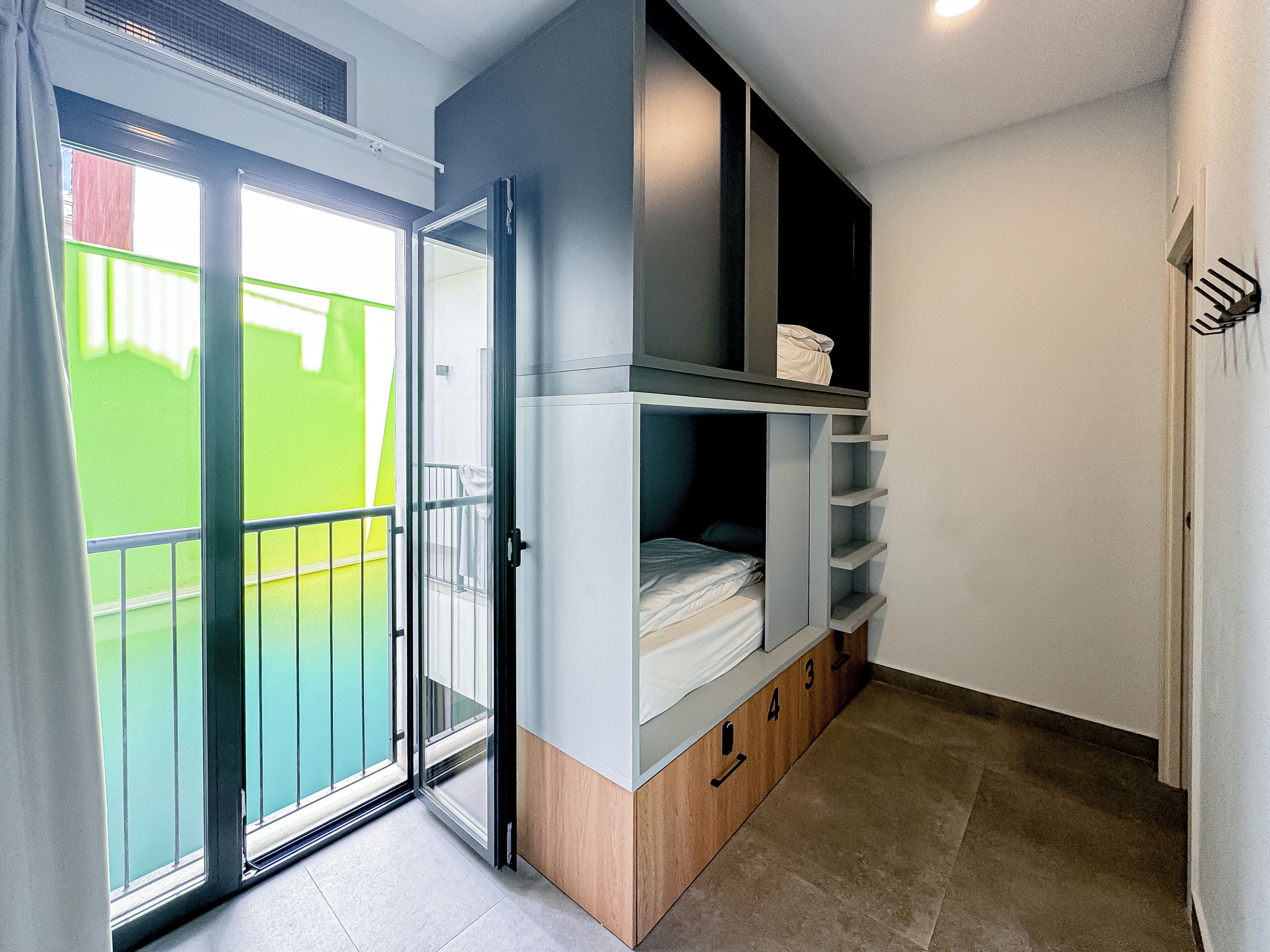 Una habitación con puerta de vidrio corredera que da a un balcón, estanterías empotradas y una cama pequeña.
