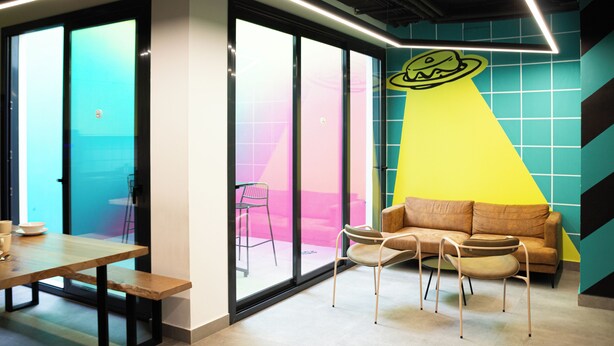 A modern interior with a glass partition, a wooden table, two chairs, a sofa, and a wall with a geometric pattern. - Funker Hostel (Málaga)