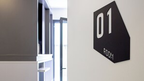A modern interior with a door labeled '01 ROOM' leading to a bright space with natural light and a view of a staircase. - Funker Hostel (Málaga)