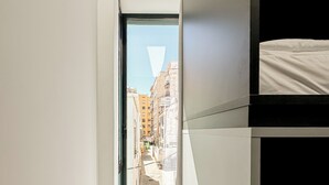 A narrow hallway with a door leading to an outdoor area, a bunk bed, and a view of buildings through the door. - Funker Hostel (Málaga)