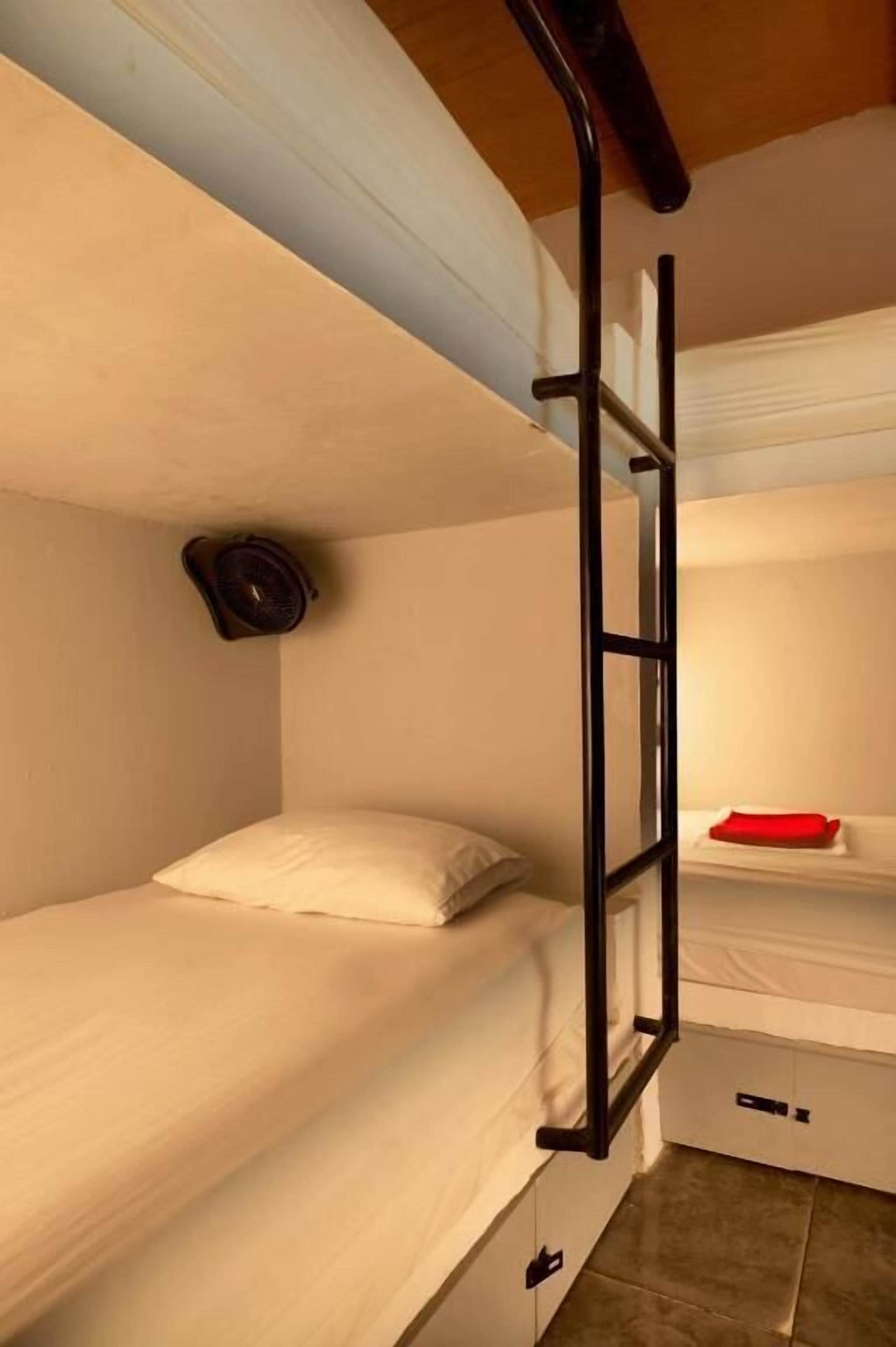 Ein Schlafzimmer mit Etagenbetten, einer Leiter, einem Ventilator und einem roten Kissen.