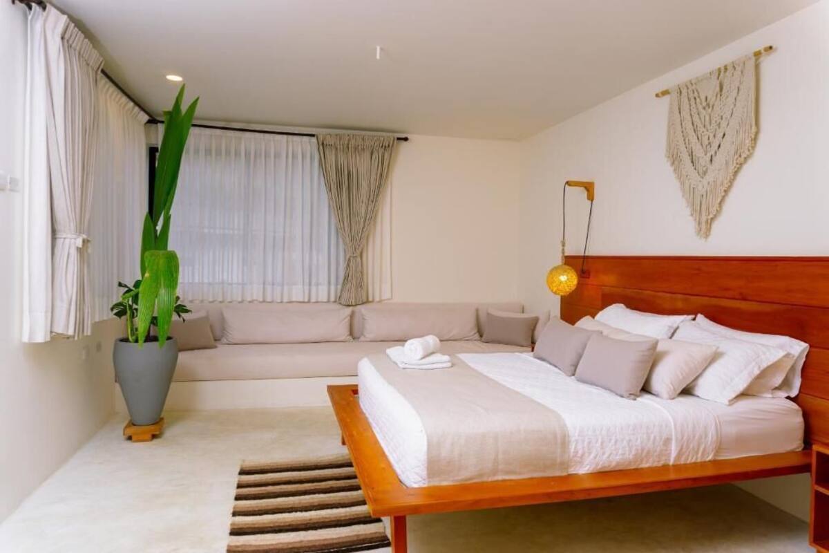 A bedroom with a wooden bed, a sofa, a potted plant, and a wall-mounted lamp.