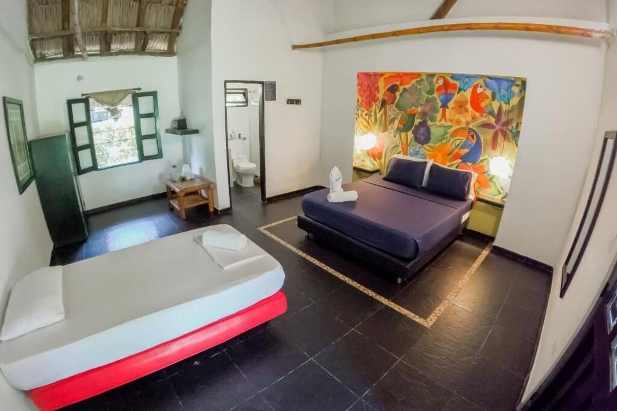 A room with a bed, a small table, a chair, a painting on the wall, and a window with a curtain.