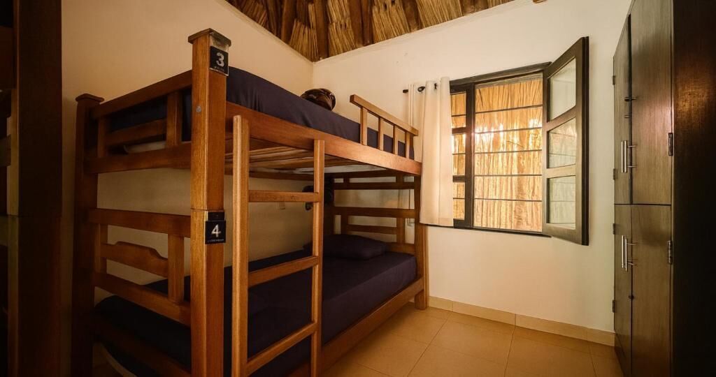 Habitació amb literes, un panell de fusta al capçal, una finestra amb cortines i un armari.