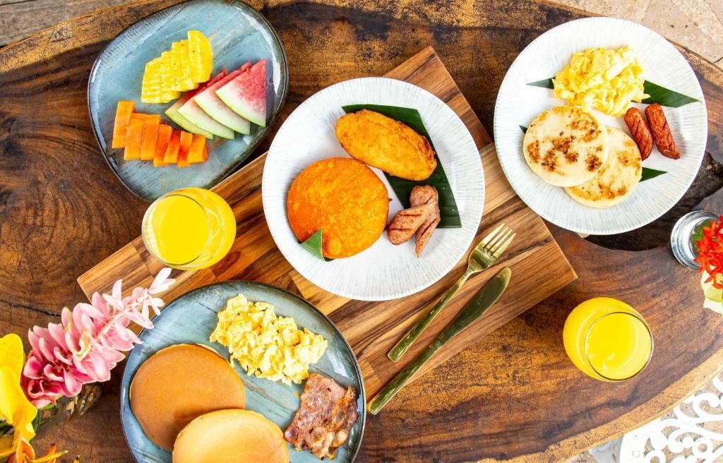 A breakfast spread with various dishes on plates, including pancakes, scrambled eggs, and fresh fruit.