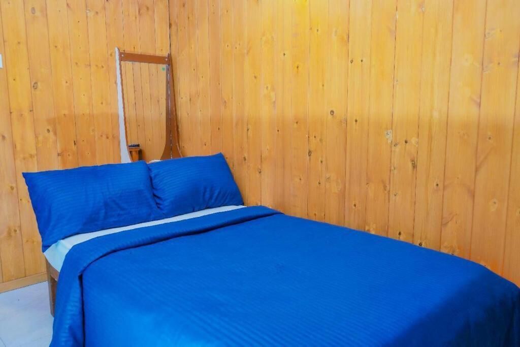 Una cama individual con ropa de cama azul en una habitación con paredes de madera.