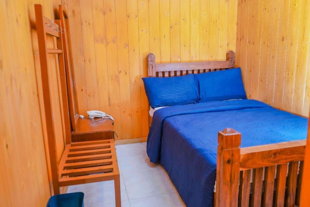 Quarto de madeira com uma cama, uma cadeira de madeira e uma pequena mesa com um telefone.