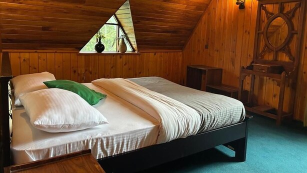 A wooden-paneled room with a bed, a small window, and a wall-mounted lamp. - Jaithra Inn (Nuwara Eliya)