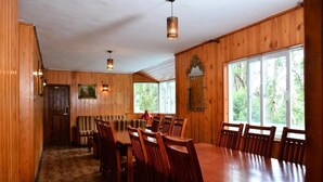 A wooden-paneled dining area with a large table and chairs, a mirror, and a window with a view of trees. - Jaithra Inn (Nuwara Eliya)