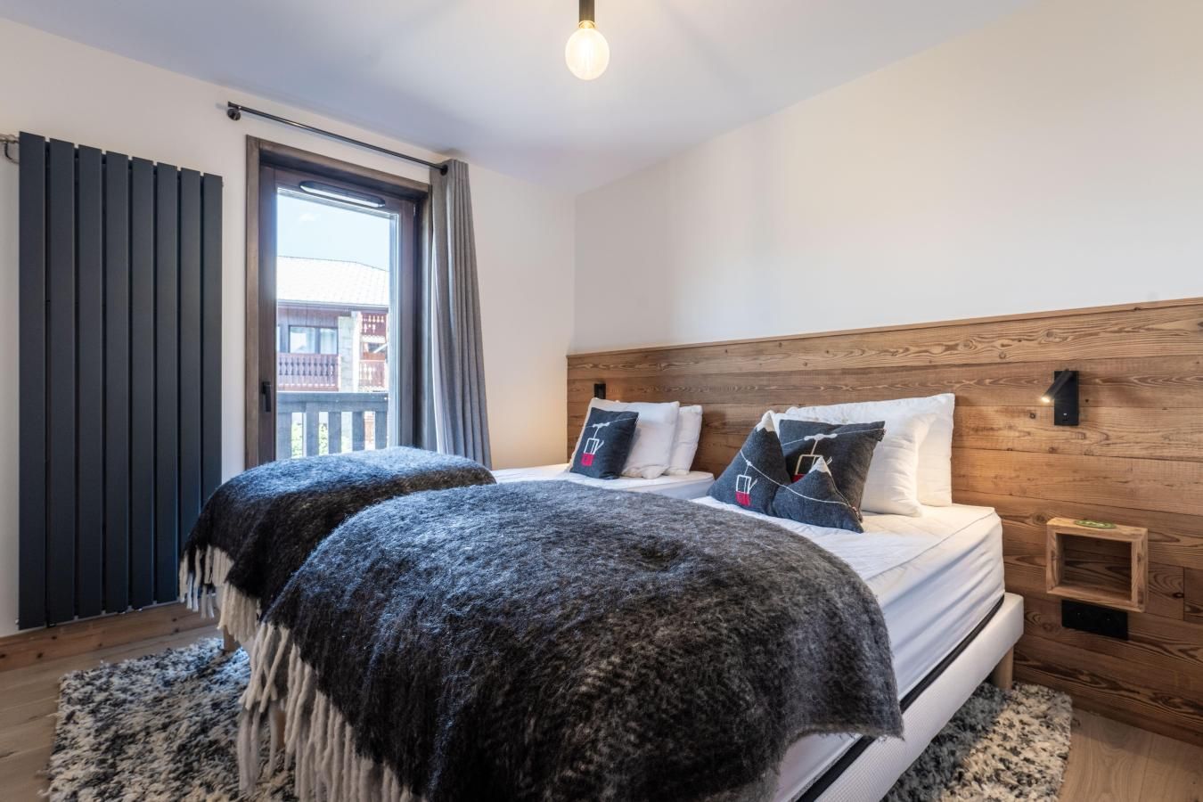Ein Schlafzimmer mit zwei Betten, einem Holz-Kopfteil, einem Fenster mit Vorhängen und Blick auf Gebäude.