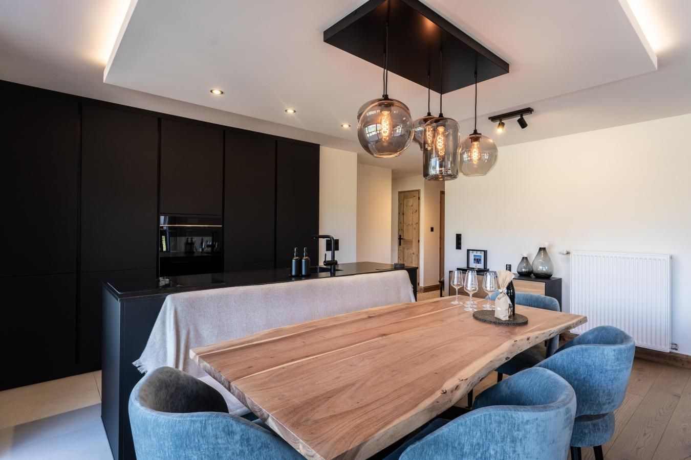 Une cuisine moderne avec des meubles de couleur sombre, une table à manger en bois et des chaises recouvertes de tissu bleu.