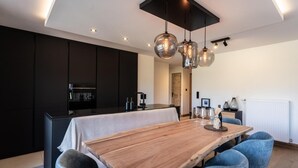 Een moderne keuken met donkere kastjes, een houten eettafel en blauwe bekleden stoelen.