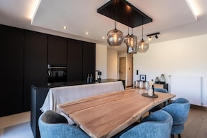 A modern kitchen with dark cabinetry, a wooden dining table, and blue upholstered chairs. - 100m from ski slopes, Ground floor, view open/resort/mountain, balcony, parking, tv, ski locker (La Plagne)
