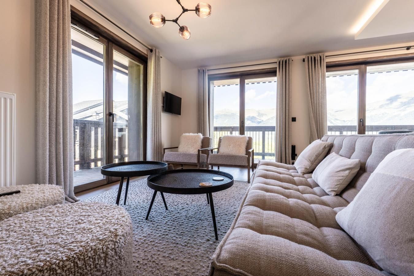 A modern living room with a sofa, two round tables, and a view of mountains through large windows.