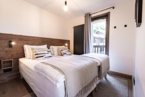 A bedroom with a wooden headboard, a large bed with multiple pillows, a bedside table, and a view of the outside through a window. - 100m from ski slopes, Ground floor, view open/resort/mountain, balcony, parking, tv, ski locker (La Plagne)