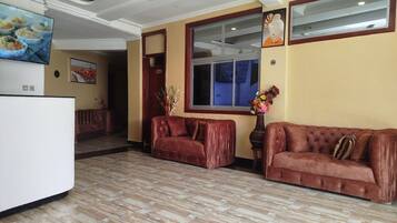 A spacious lobby with a wooden floor, a brown leather sofa, a white reception desk, and a large window.