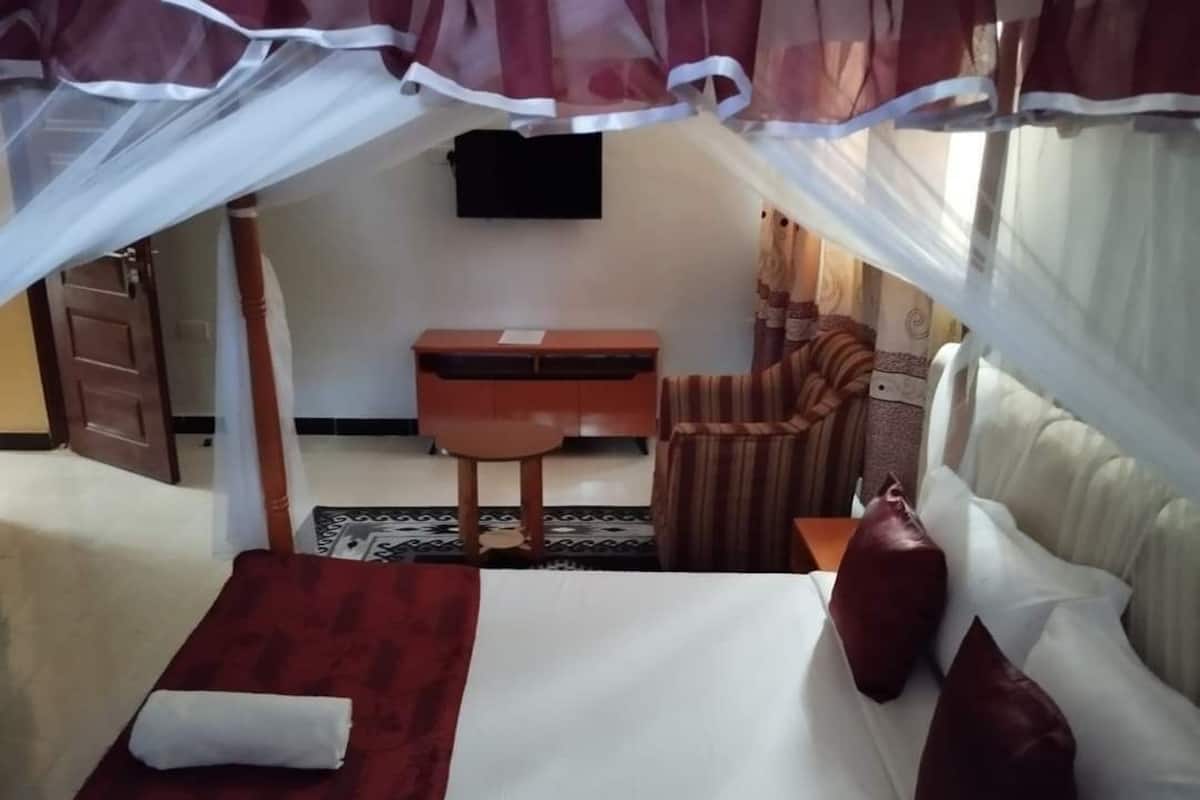 A bedroom with a bed, a desk, a chair, and a TV.