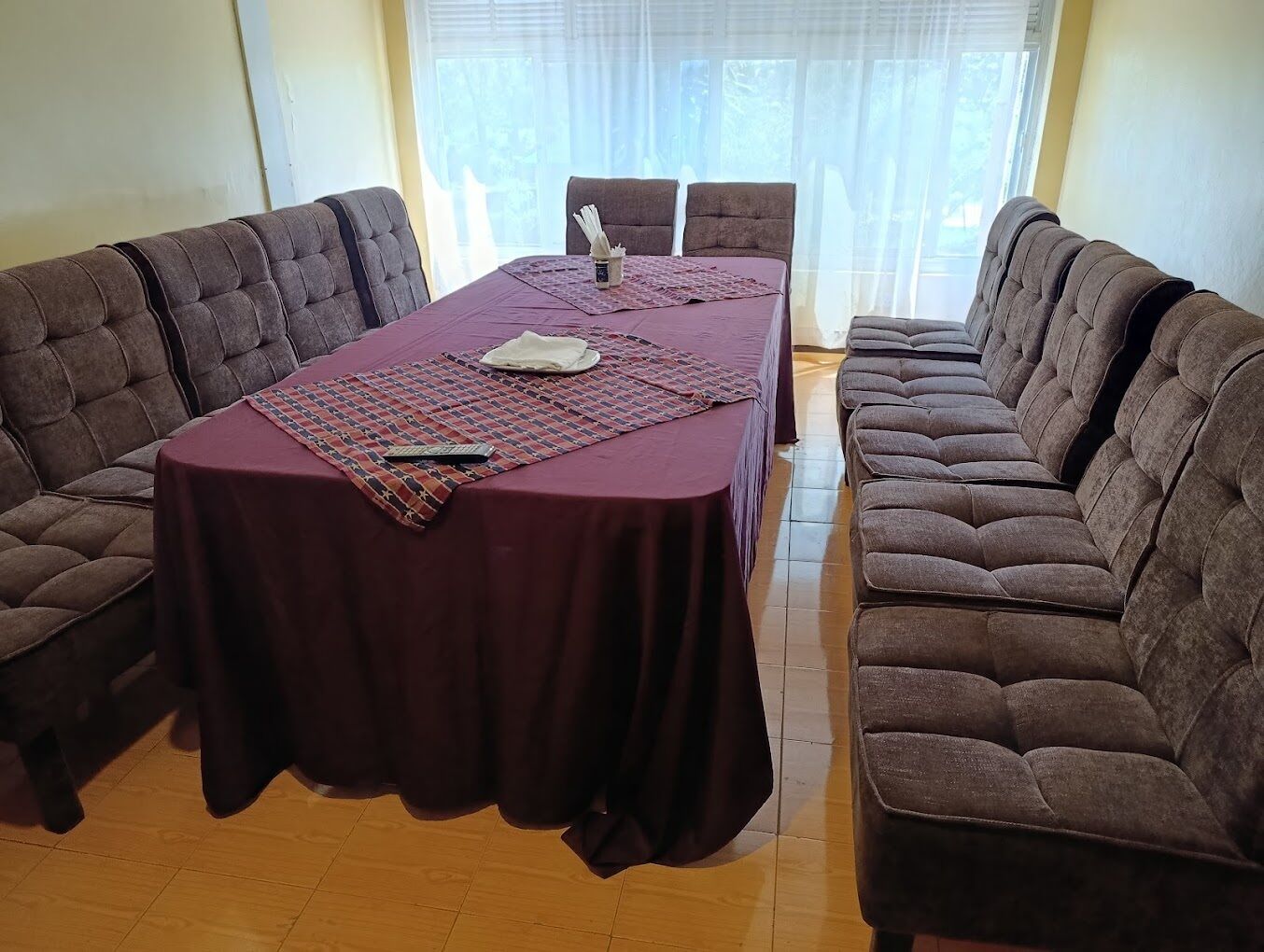 A conference room with a rectangular table covered by a dark tablecloth, surrounded by two rows of brown upholstered chairs.