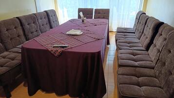 A conference room with a rectangular table covered by a dark tablecloth, surrounded by two rows of brown upholstered chairs.
