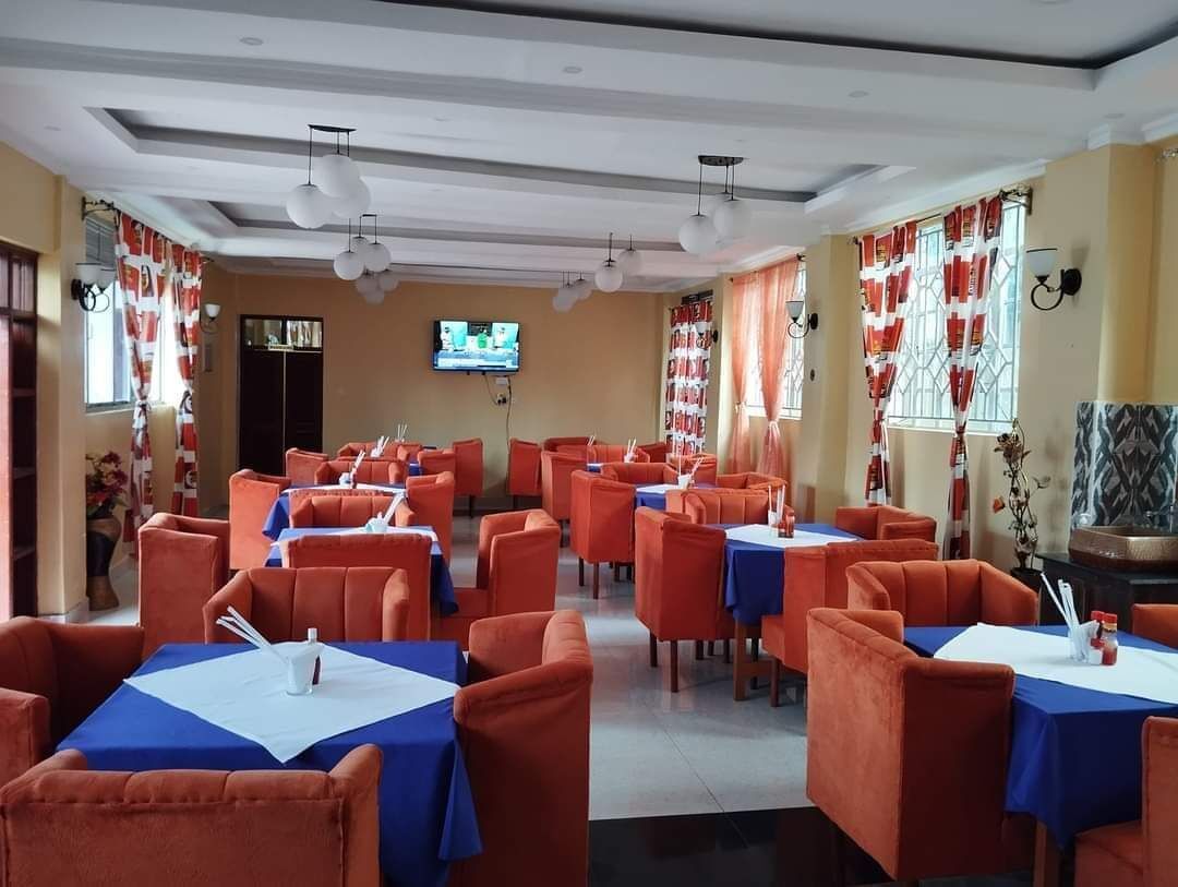 A restaurant with multiple tables and orange chairs, a television on the wall, and red and white curtains.