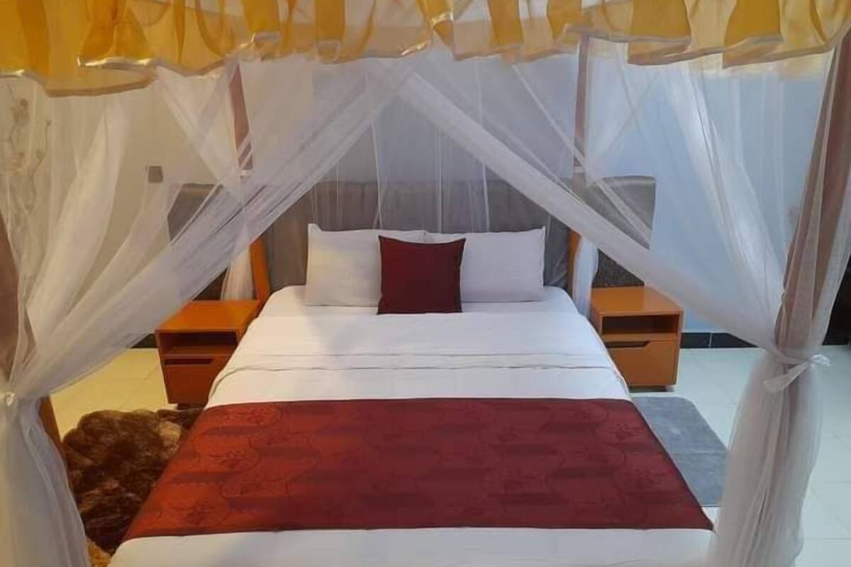 A bed with a canopy, white bedding, and a red throw blanket.