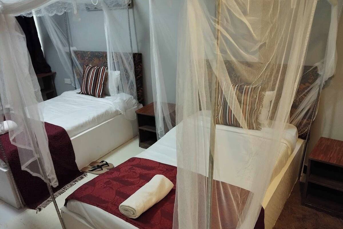 A room with two beds, each covered with a canopy. There is a red bedspread on one bed and a white one on the other.