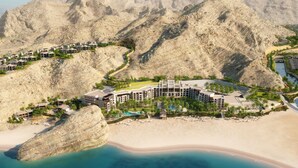 A resort with multiple buildings, a beach, and a large rock formation. - Jumeirah Muscat Bay (Bandar Jissah)