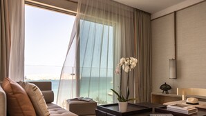 A modern hotel room with a large window, a sofa, a coffee table, and a potted orchid. - Jumeirah Muscat Bay (Bandar Jissah)