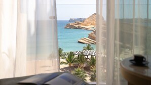 A room with a view of a beach and cliffs through sheer curtains. - Jumeirah Muscat Bay (Bandar Jissah)