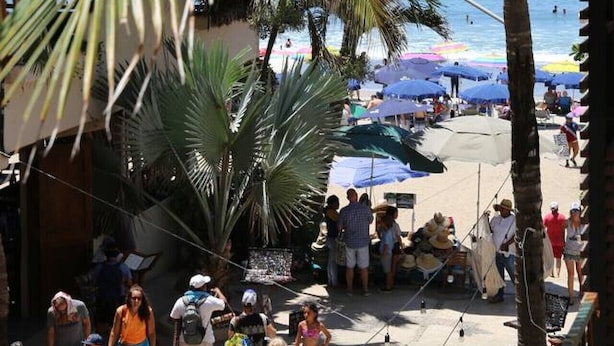 Une promenade en bord de mer bordée de palmiers, avec des parasols de plage et des gens qui se promènent.