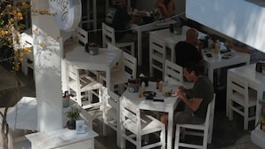 Un espace de restauration en plein air avec des tables et des chaises blanches, un présentoir à menus et une enseigne portant le nom « Mati ».