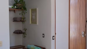 Une pièce avec une porte en bois, un banc sur lequel sont pliées des serviettes, des étagères avec des serviettes et une plante, et un tableau encadré accroché au mur.