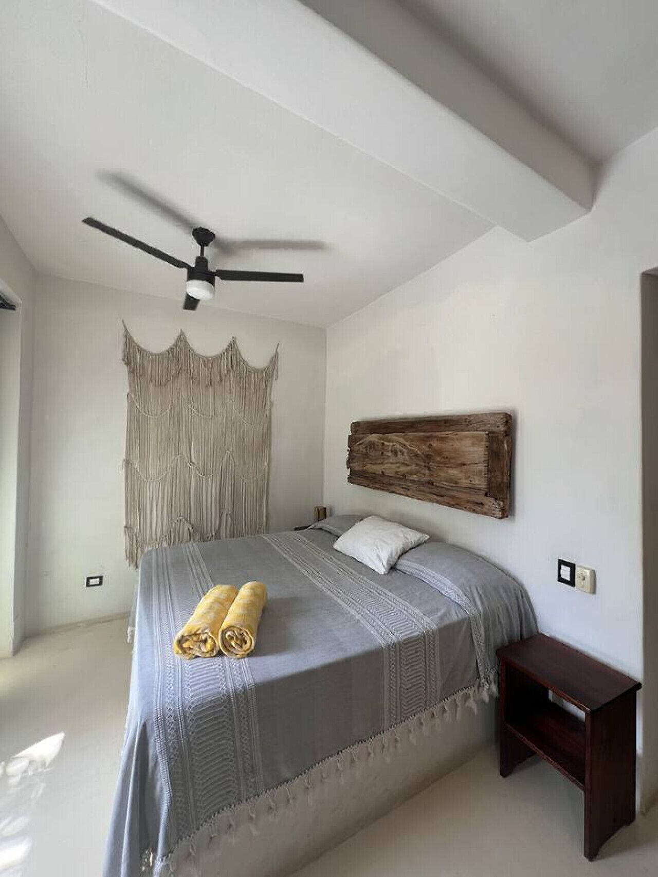 Una camera da letto con un letto, una ventola a soffitto, una testiera in legno fissata al muro e un comodino.