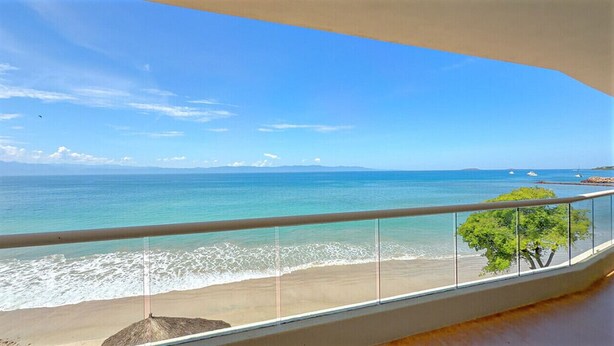 Un balcon avec vue sur l’océan et un arbre.