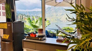 A kitchen with a view of a lake and mountains, a refrigerator, and a stove with a stack of plates. - Luxury Atitlan Suites (San Pedro La Laguna)