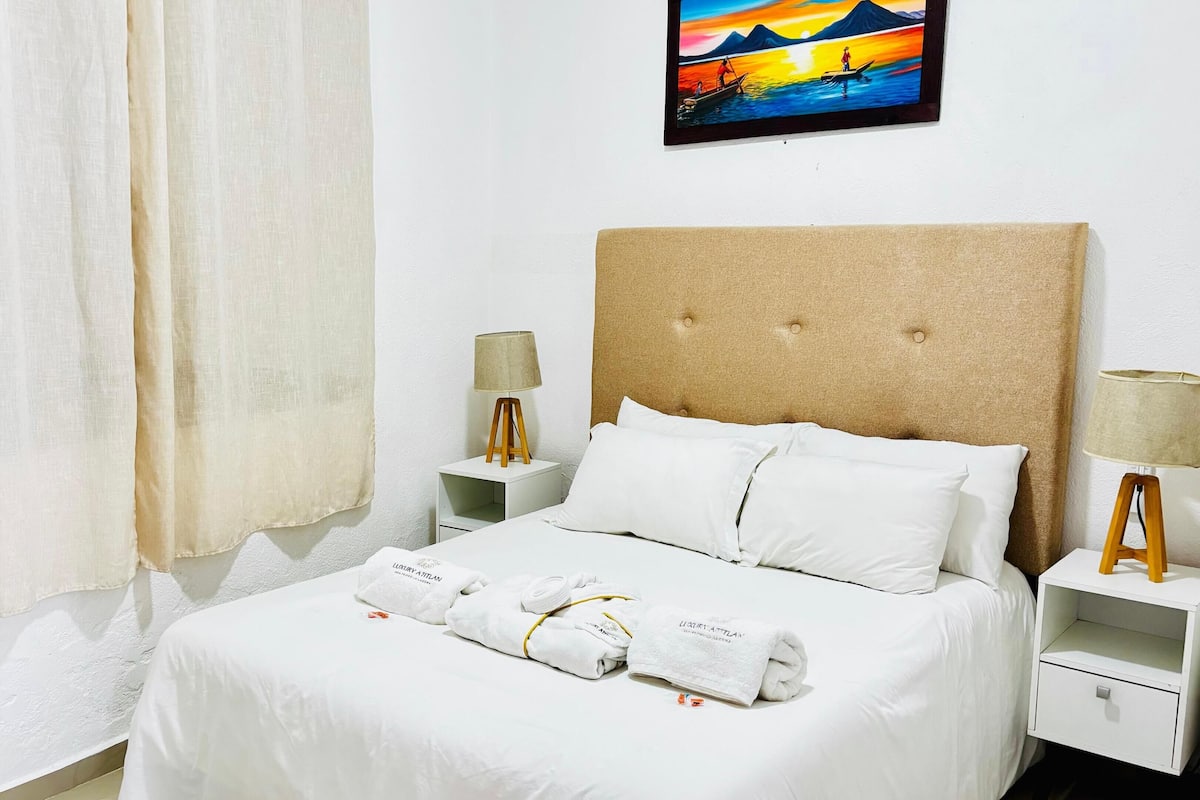 A neatly made bed with white linens and towels, a wooden headboard, and two bedside tables with lamps.