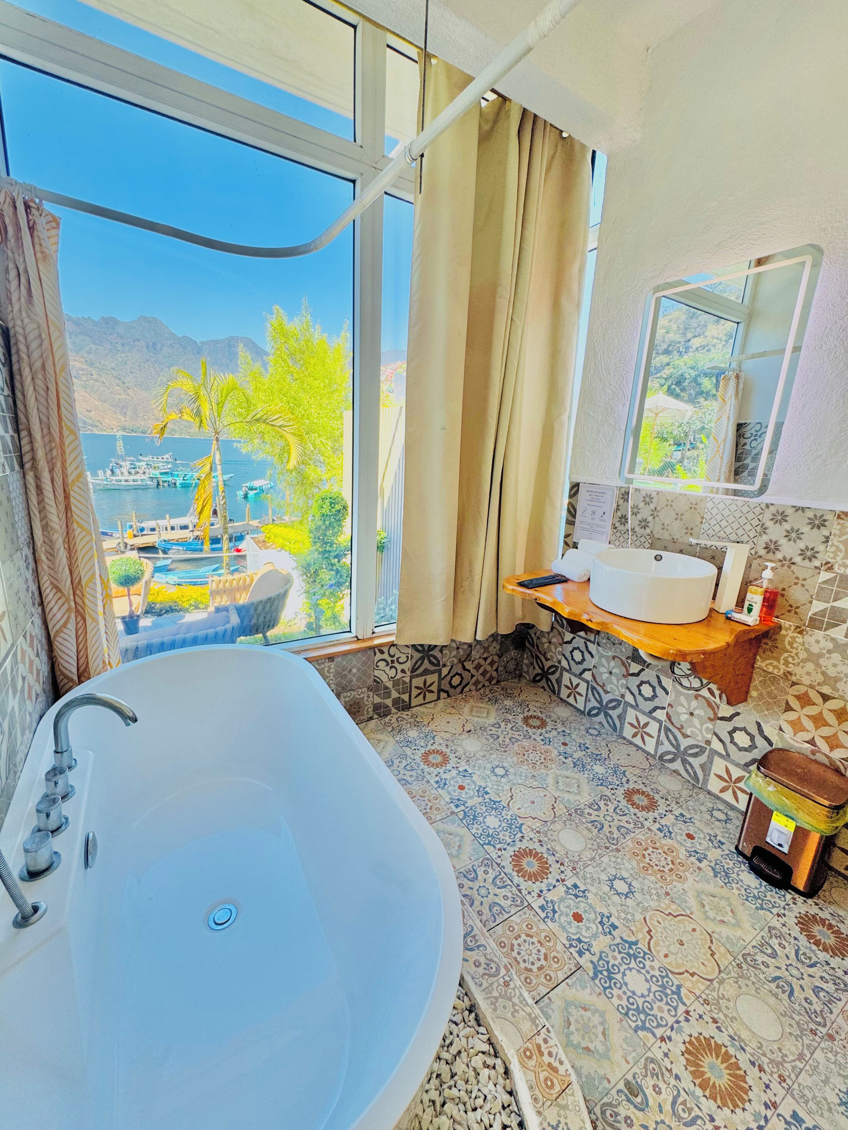 A bathroom with a large bathtub, a sink, and a window offering a view of boats and mountains.