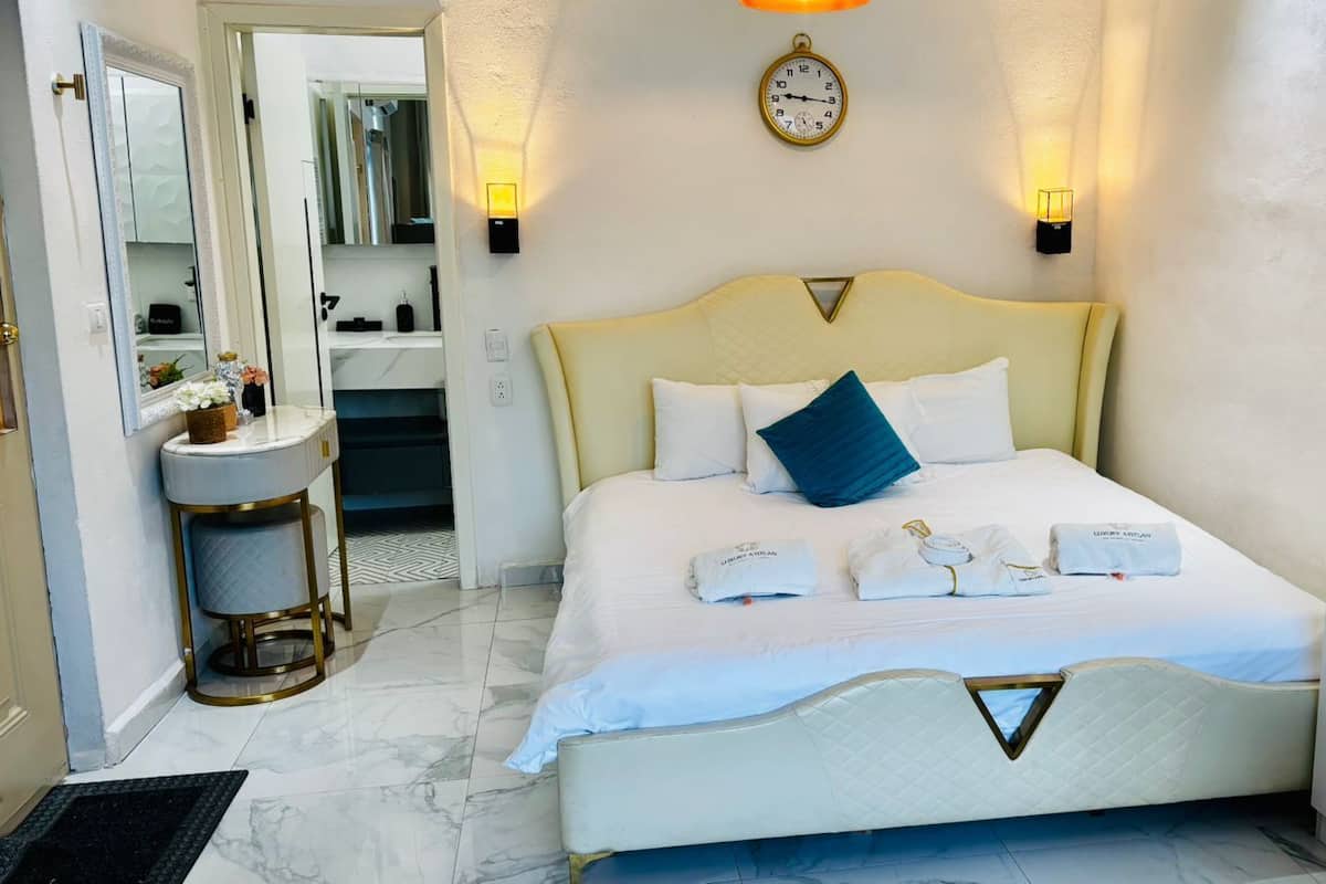 A hotel room with a bed, bedside lamps, a clock, and a bathroom visible through an open door.