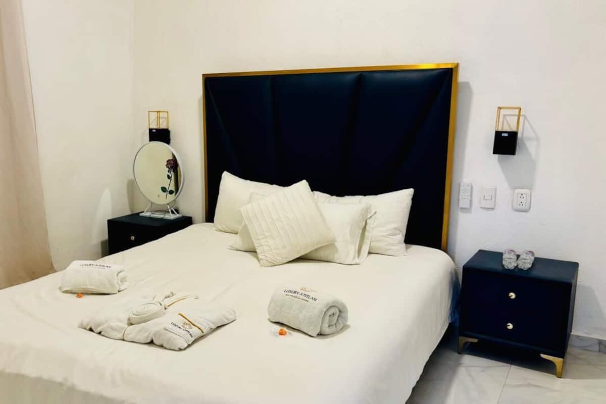 A neatly made bed with white linens and pillows, a bedside table with a mirror, and a small nightstand with a power strip.