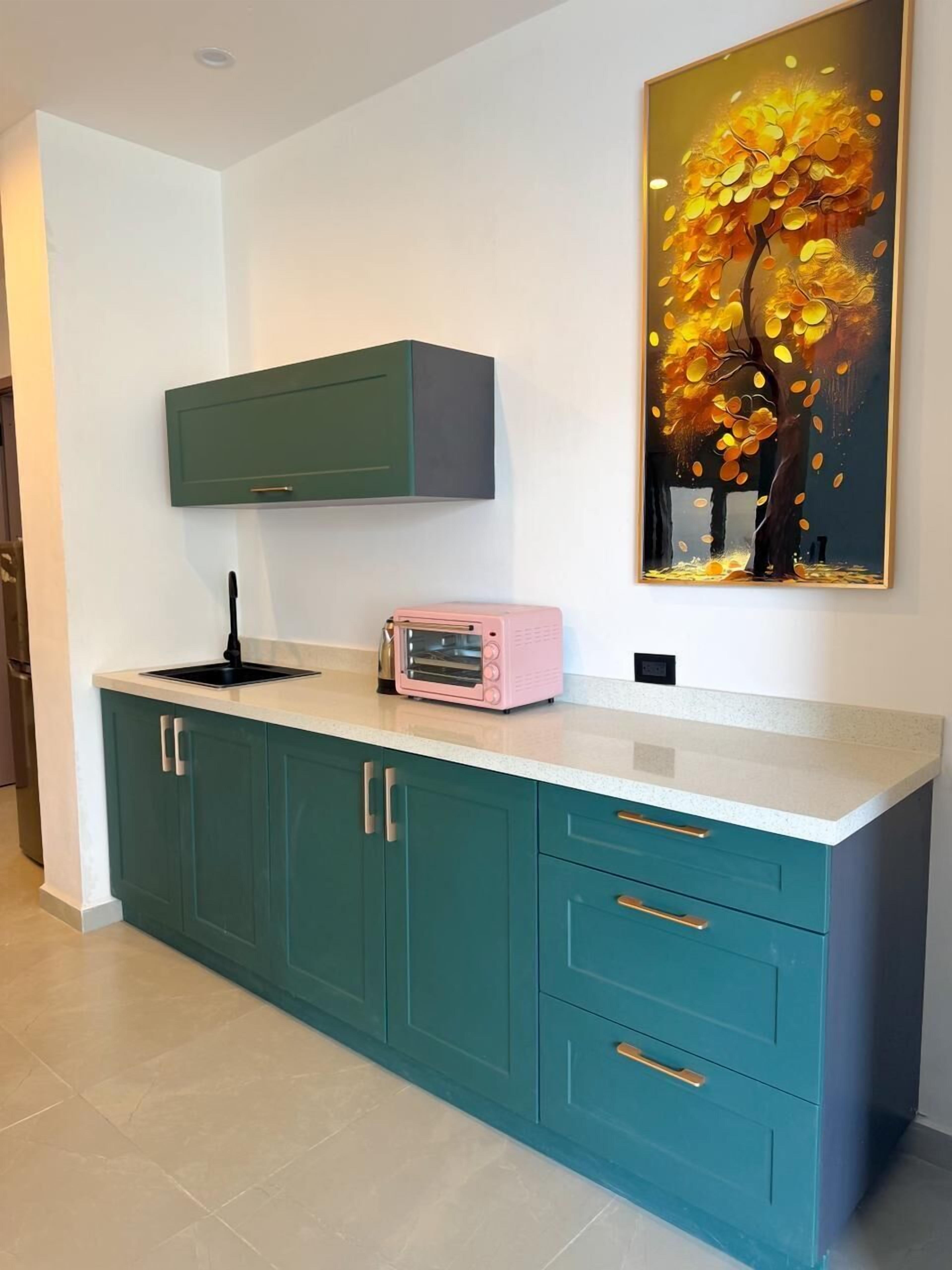 A kitchen with teal cabinets, a white countertop, a pink toaster oven, and a wall-mounted cabinet above the sink.