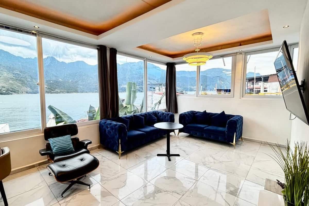 A modern room with a large window offering a lake view, a sofa, a chair, and a small table.