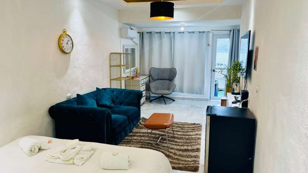 Una habitación de hotel con una cama, un sofá azul, un sillón gris, una mesita y un televisor.