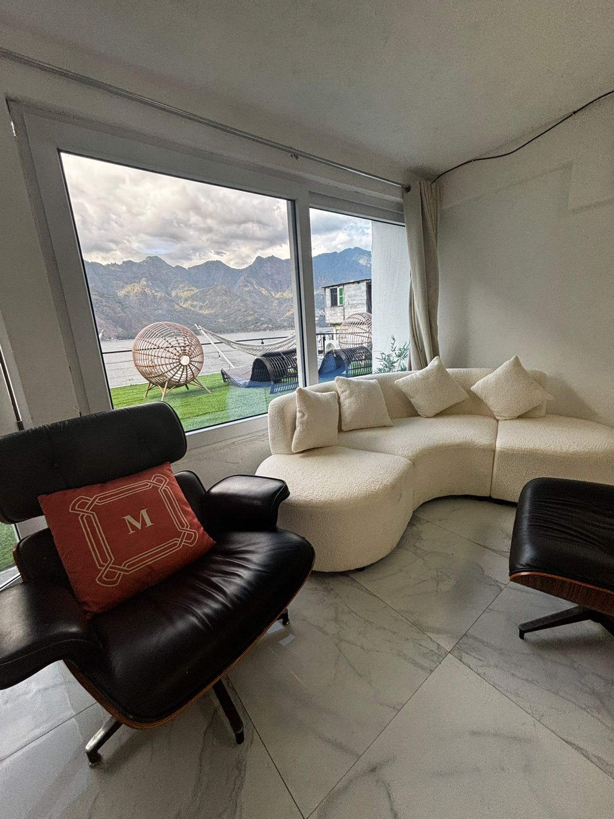 A modern living room with a curved sofa, a black leather chair, and a view of mountains through large windows.