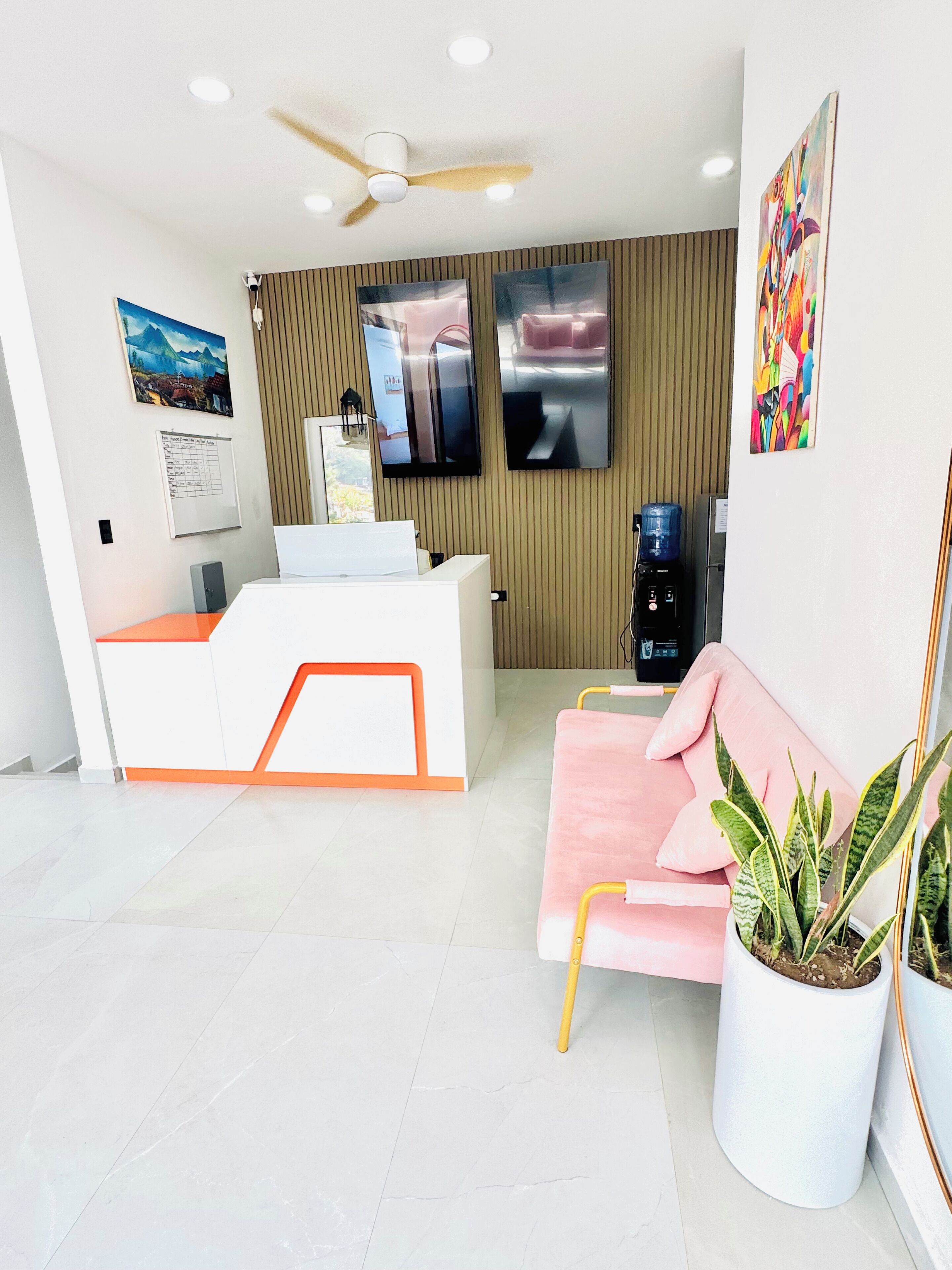 Un área de recepción moderna con un mostrador blanco, un sofá rosa y un ventilador de techo.