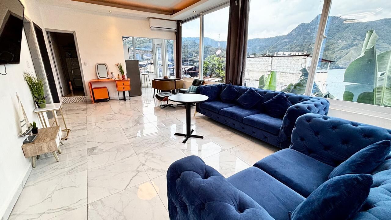 A modern living room with a blue sofa, a small round table, and a view of mountains and water.